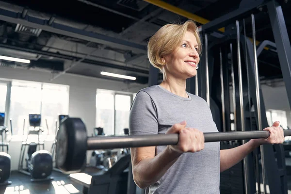 Mujer alegre haciendo ejercicio con barra en el gimnasio — Foto de Stock