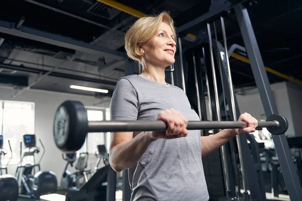 Mujer alegre haciendo ejercicio con barra en el gimnasio — Foto de Stock