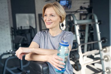 Spor salonunda elinde bir şişe suyla neşeli bir kadın.