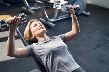 Sportif kadın spor salonunda dambıllarla egzersiz yapıyor.