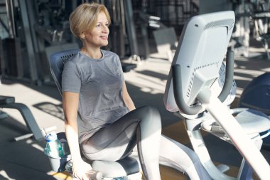 Spor salonunda spor aletleri kullanan neşeli bir kadın.