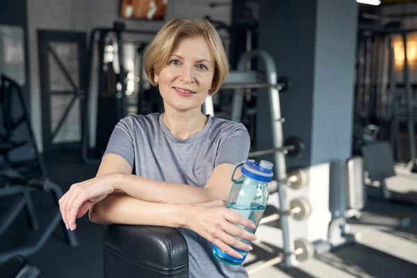 Radosna kobieta z butelką wody stojąca na siłowni — Zdjęcie stockowe