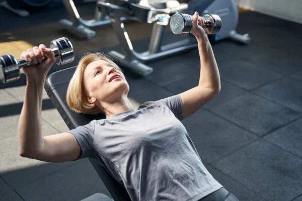 Sportif kadın spor salonunda dambıllarla egzersiz yapıyor.