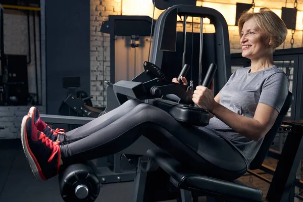 Mujer sonriente usando la máquina de fitness en el gimnasio — Foto de Stock