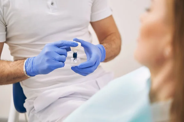 Дантист показывает зубной имплантат женщине в клинике — стоковое фото