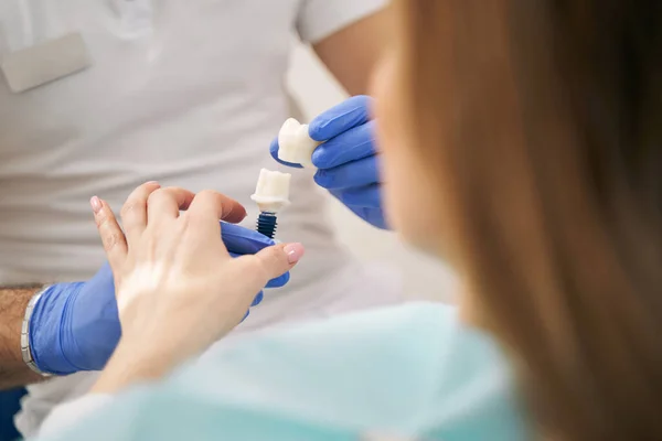 Dentista mostrando implante dental a mujer en clínica —  Fotos de Stock