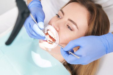 Klinikte dişçi kadın dişlerini diş aletleriyle muayene ediyor.