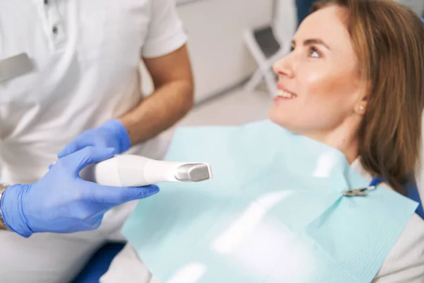 Dentista con dispositivo dental sentado al lado de la mujer en la clínica —  Fotos de Stock