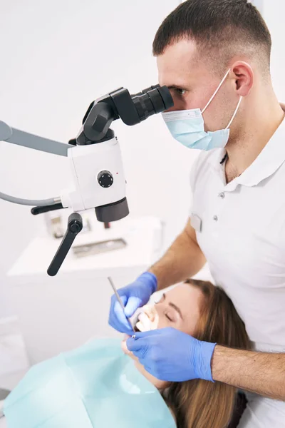 Οδοντίατρος που εκτελεί οδοντιατρική θεραπεία με μικροσκόπιο στην κλινική — Φωτογραφία Αρχείου