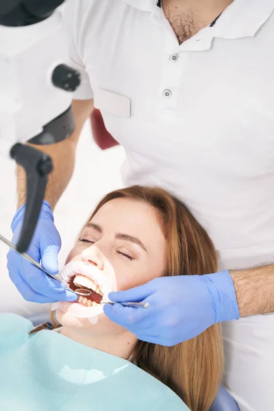 치과의 사는 현미경 과 치아 도구를 사용하여 여자 치아를 검사한다 — 스톡 사진