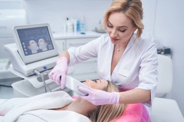 Deneyimli kozmetolog, müşteri tenini ultrasonla sıkıyor.