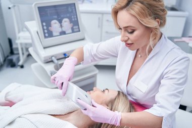 Odaklanmış dermatolog hastaya ultrason uyguluyor.