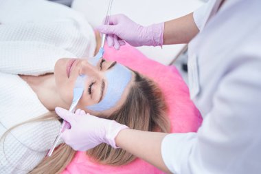 Dermatolog genç bir kadının yüzüne maske takıyor.