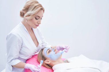 Hasta yüzüne maske takan konsantre cilt doktoru