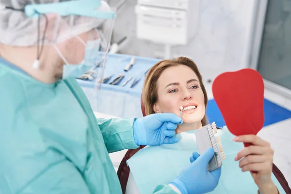 Dentiste masculin choisissant la couleur des dents de la femme avant le traitement dentaire — Photo