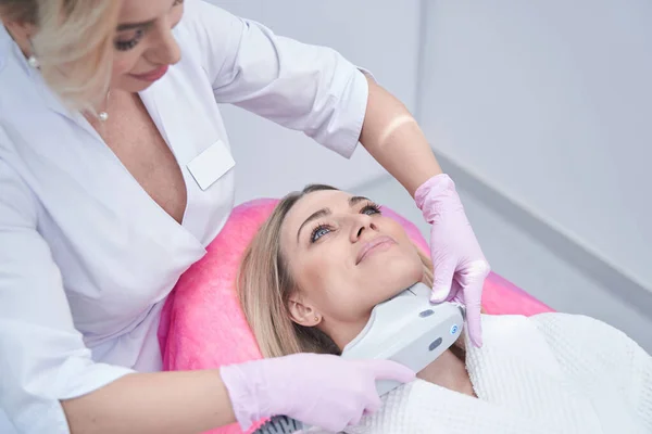 Lékař lisování ultrazvukové zařízení proti ženě bradu během kosmetické procedury — Stock fotografie