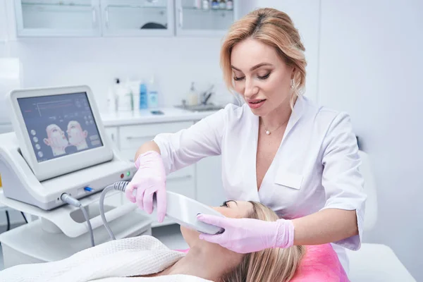 Dermatólogo concentrado realizando procedimiento de belleza con dispositivo ultrasónico — Foto de Stock