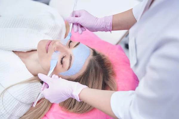 Dermatólogo aplicando mascarilla a cara de mujer joven — Foto de Stock