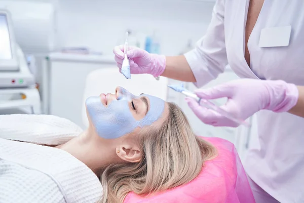 Dermatólogo que cubre la piel facial del cliente con pasta de arcilla azul — Foto de Stock