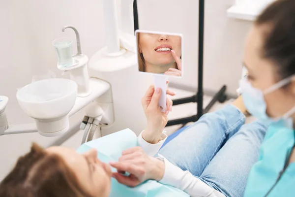 Mujer mirando en el espejo en la clínica dental —  Fotos de Stock