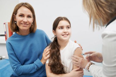 Gülümseyen küçük kız klinikte aşı yaptırıyor.
