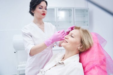 Güzellik kliniğinde oturan mutlu, olgun bir hasta.