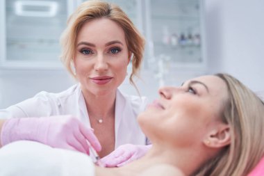 Deneyimli bir dermatolog hastanın dekolte bölgesine deri doldurucu enjekte ediyor.