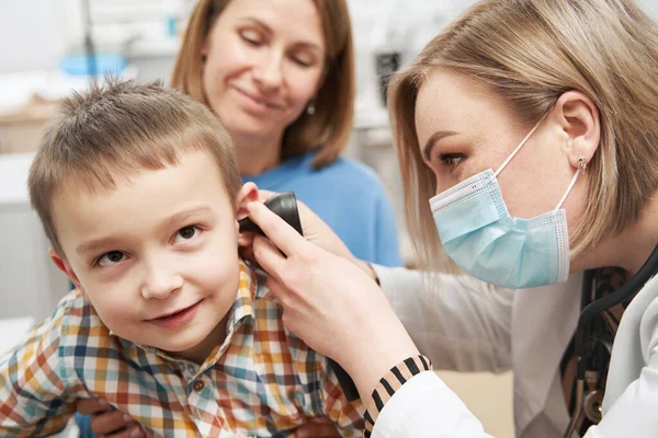 Pediatra examinando oído de niño pequeño con otoscopio en clínica — Foto de Stock
