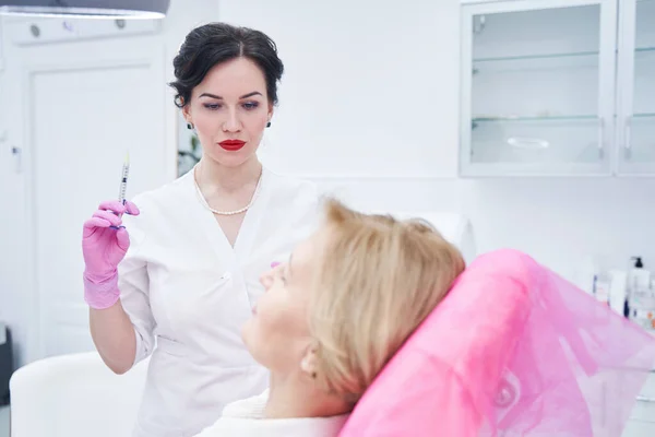 Ernstige cosmetoloog op zoek naar haar volwassen patiënt — Stockfoto