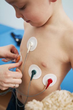Doktor, çocuk göğsüne elektrokardiyograf sensörleri yerleştiriyor.