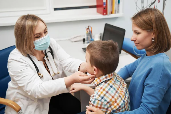 Female pediatrician examining little boy neck in clinic — ストック写真