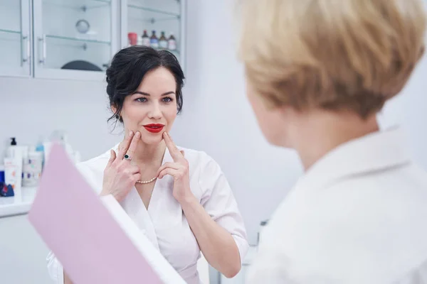 Primer plano de la joven maestra de belleza apuntando a su barbilla —  Fotos de Stock