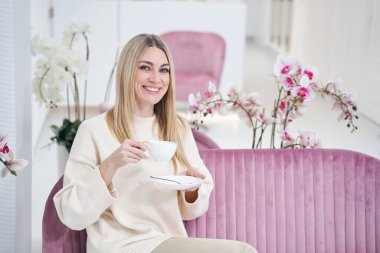 Fuayede oturmuş bitkisel içeceği olan neşeli bir güzellik salonu müşterisi.