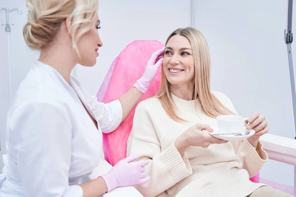 Cheerful female patient being examined by dermatologist — стоковое фото