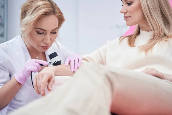 Concentrated dermatologist examining her client skin with dermoscope — Stock Photo, Image