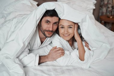 Kadın ve partneri battaniyenin altından kameraya bakıyorlar.