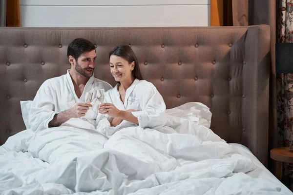 Couple clinking their glasses in bed of hotel — 스톡 사진