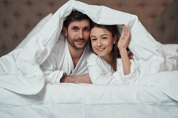 Ehepartner versteckt sich unter Decke und blickt in Kamera — Stockfoto