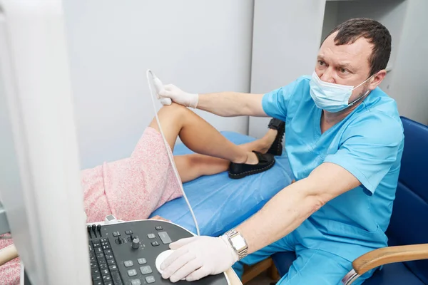 Médico caucásico realizando cuidadosamente un ultrasonido de la articulación de la rodilla — Foto de Stock