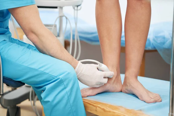 Caucasian doctor performing an ultrasound on young lady ankle joint — Foto de Stock