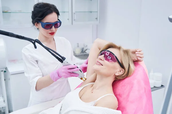 Woman receiving underarm laser hair removal treatment in clinic — стоковое фото