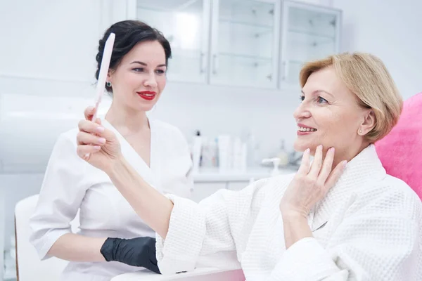 Femme heureuse regardant dans le miroir à la clinique de cosmétologie — Photo