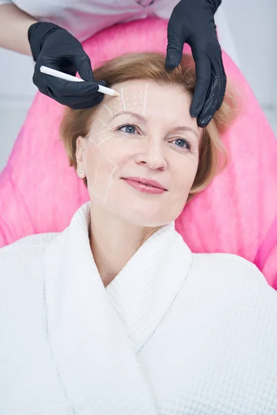 Cosmetólogo marcas de dibujo en la frente de la mujer en el salón de belleza — Foto de Stock