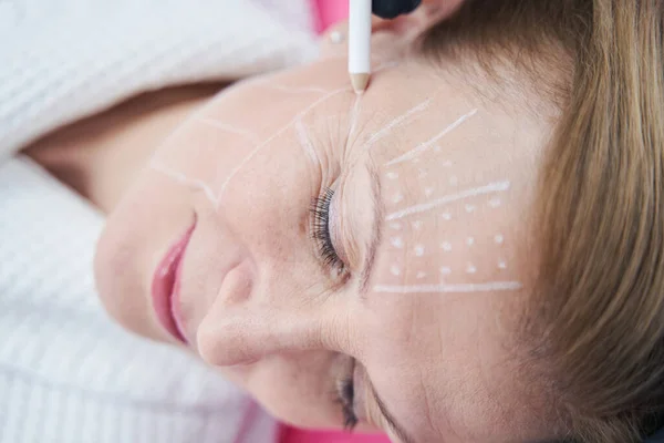 Beautician drawing line on woman face with white pencil — 스톡 사진