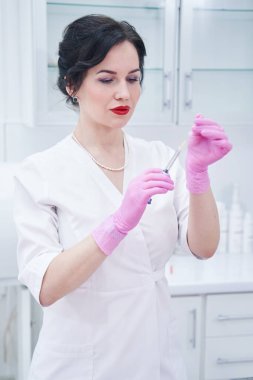 Konsantre olmuş esmer kadın, elinde sıvıyla penise bakıyor.