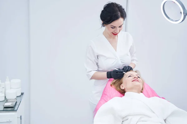 Cheerful beautician drawing marks on woman face in beauty salon — Foto de Stock
