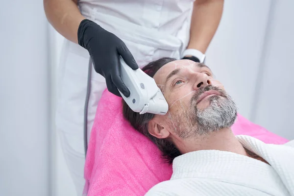 Thoughtful adult male doing face lifting in clinic — Stock Photo, Image