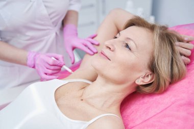 Güzellik uzmanı güzellik salonundaki kadın koltukaltına izler çiziyor.