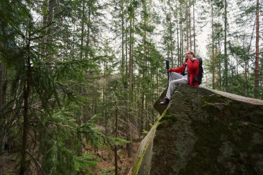 Yürüyüşçü ormanda uçurumdan cep telefonuyla konuşuyor.