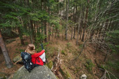 İskandinav sırıklarıyla kaya üzerinde oturan kadın turist